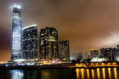 Illuminated city by river against sky at night