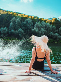 Rear view of woman sitting on pier in lake against trees