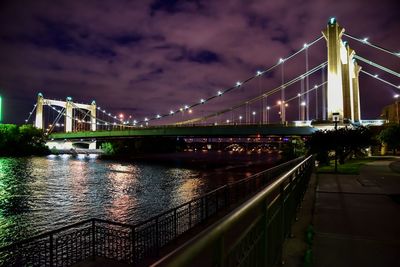 Illuminated bridge over river against cloudy sky