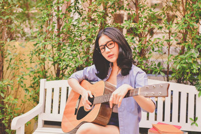 Portrait of woman playing guitar while sitting on bench in park