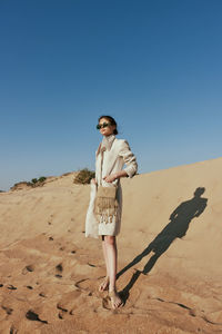 Full length of young woman standing at beach against clear sky