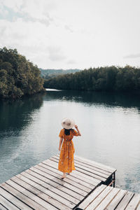 Woman standing on pier by lake against sky