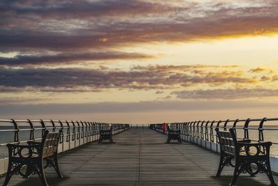 Empty bench on pier over sea against sky during sunset