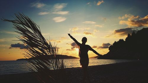 Silhouette woman standing at beach against sky during sunset