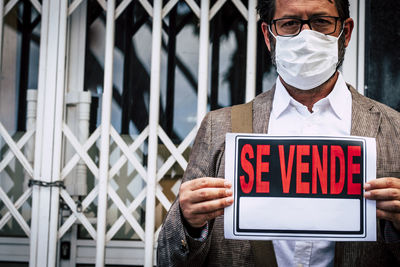 Man wearing face mask holding paper with text against built structure