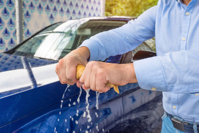 A mans hands are twisting a wet cloth at the car background