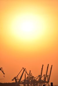 Silhouette cranes at construction site against orange sky