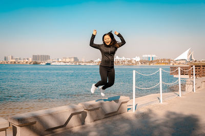 Full length of happy young woman jumping by sea