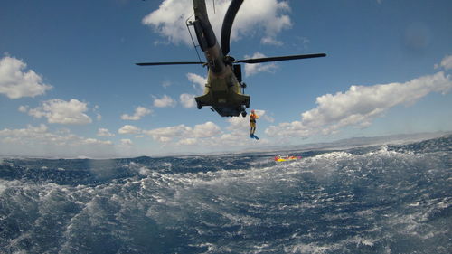 Person jumping in sea from helicopter against sky