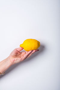 Cropped image of hand holding fruit against white background