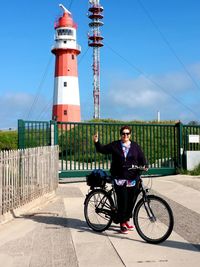 Woman riding bicycle by lighthouse against sky