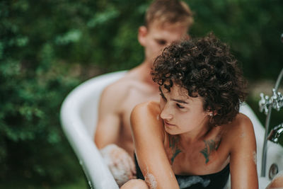 Midsection of shirtless young woman sitting outdoors
