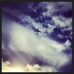 Low angle view of airplane flying against cloudy sky