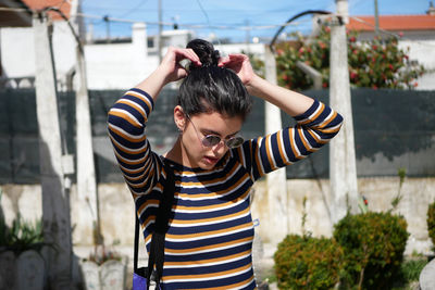 Young woman tying hair bun while standing in terrace