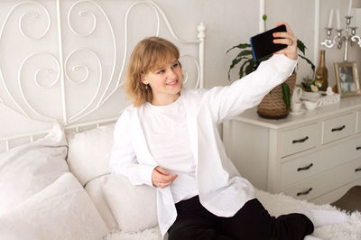 Portrait of young woman with arms crossed standing on bed at home