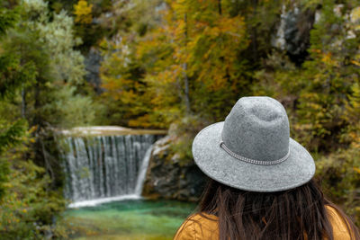 Rear view of woman looking at stream with waterfall in autumn forest
