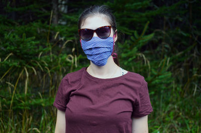 Portrait of young woman with brown ponytail in colorful face mask in sin glasses, nature background