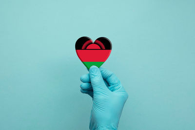 Midsection of person holding heart shape against blue background