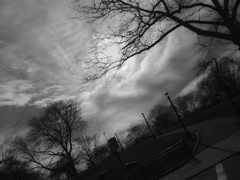 Low angle view of bare trees against cloudy sky