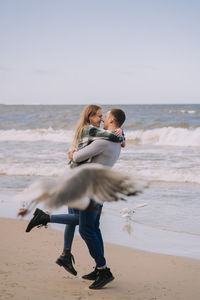 Close up of couple kissing and hugging near the sea and looking to each other.