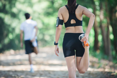 Rear view of woman and man stretching leg while exercising on road