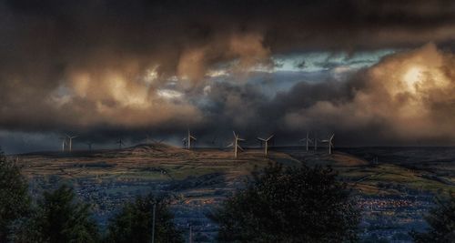 Wind turbines on landscape against cloudy sky