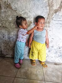  sister touching cheek of brother while standing against wall