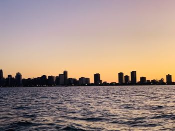 Sea by buildings against clear sky during sunset