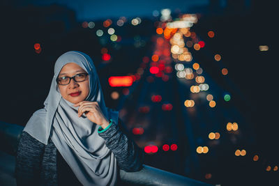 Portrait of woman standing in hijab against illuminated city at night