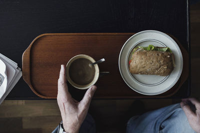 Low section of senior man having tea and sandwich at table