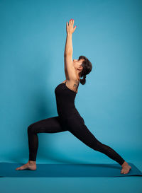 Full length of woman exercising against blue background