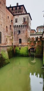 Arch bridge over canal amidst buildings against clear sky