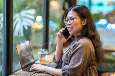 Young woman using mobile phone while sitting on table
