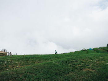 Low angle view of grassy field against cloudy sky