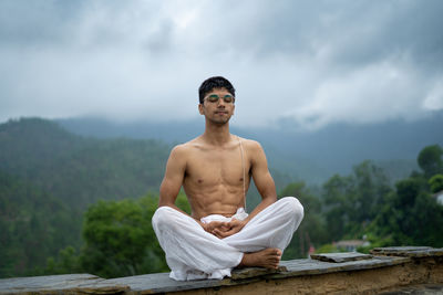 Full length of shirtless man sitting against sky