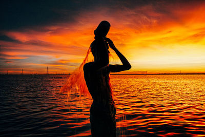 Silhouette man standing on sea against orange sky