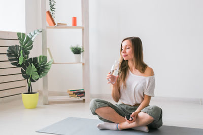 Full length of woman sitting while drinking at home