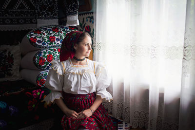 Thoughtful woman looking through window curtain