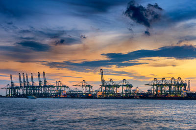 Silhouette cranes at commercial dock against sky