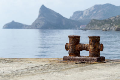 Close-up of rusty metallic structure in sea against mountains
