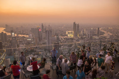 Group of people in city against sky during sunset