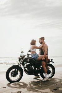 People riding motorcycle on beach against sky