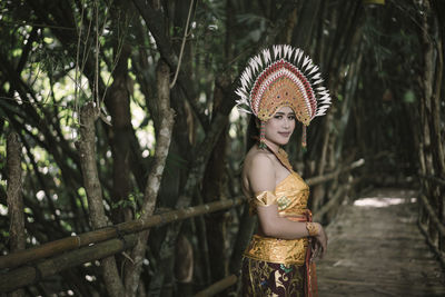 Portrait of woman wearing traditional clothing standing on boardwalk amidst trees