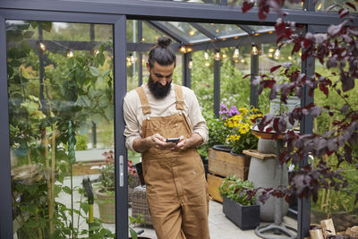 Man using cell phone in front of greenhouse