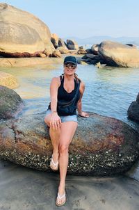 Portrait of smiling woman sitting on rock by beach