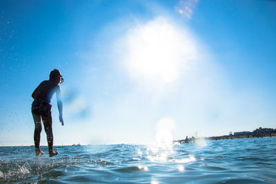 Optical illusion of boy standing on sea against blue sky during sunny day