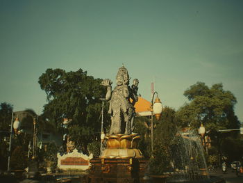 Statue against trees and plants against sky