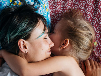 Close-up of smiling mother sleeping with daughter on bed