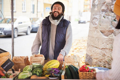 Smiling man buying fresh vegetables from female market vendor at fruit stall