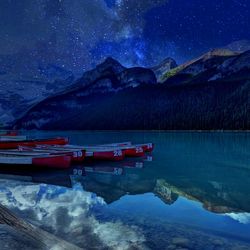 Boat moored in lake against snowcapped mountains at night